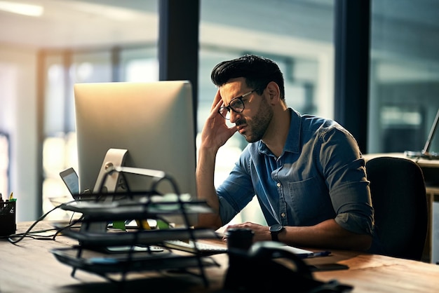 Business man with a stress headache feeling tired pain and stressed while working on a computer Young male office worker work on a deadline late at night IT technology guy looking upset