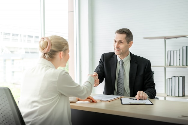 Business man and woman shaking hands on desk after job interview in meeting room at office