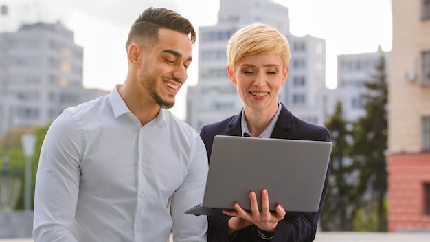 Business man and women standing near business center at street looking at laptop discuss project