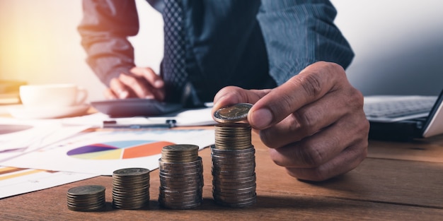 Business man working and writing on notebook with stack of coins for financial and accounting concept.