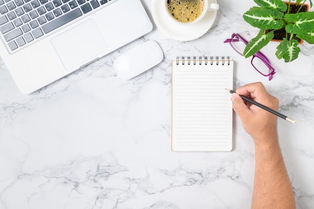 Uomo di affari che scrive sul taccuino in bianco con il computer portatile e caffè sulla tavola di marmo. concetto di posto di lavoro