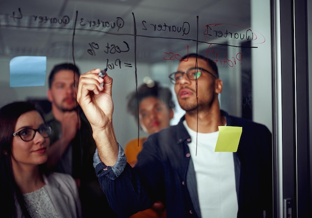 business man writing on transparent glass wall with coworkers standing by in office