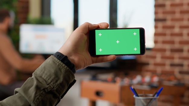 スマートフォンで水平方向のグリーンスクリーンを保持し、ディスプレイ上の空白のクロマキーコピースペースを見ているビジネスマネージャー。電話で分離されたモックアップテンプレートまたは背景を使用します。閉じる。