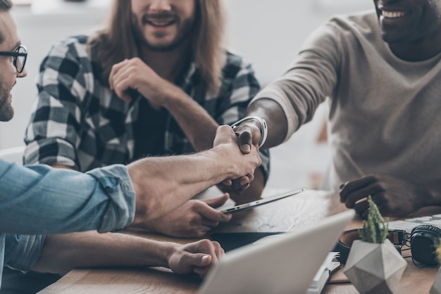 Incontro di lavoro. primo piano di giovani che comunicano tra loro in ufficio mentre due uomini si stringono la mano e sorridono