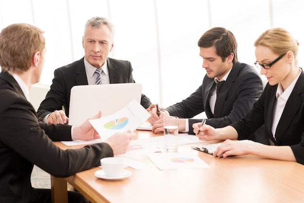 Business meeting. Four business people in formalwear discussing something while sitting together at the meeting