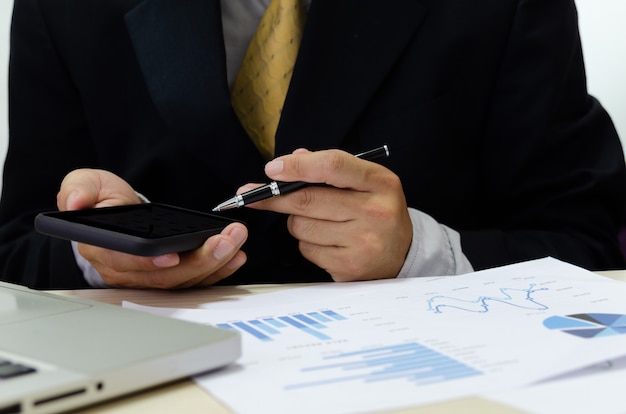 Business men hand holding cell phones and pens on the desk have business documents graphs financial reports