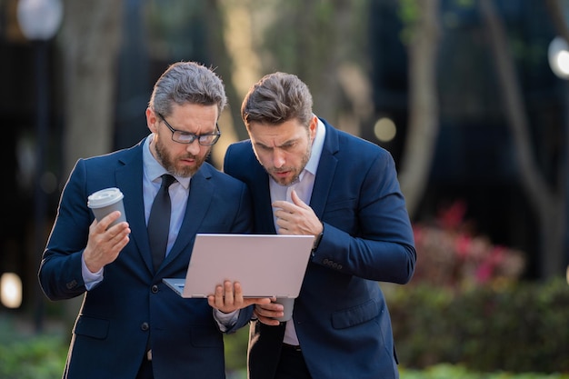 Business men team using laptop outdoor colleagues in suit talking outdoor businessmen discussing out