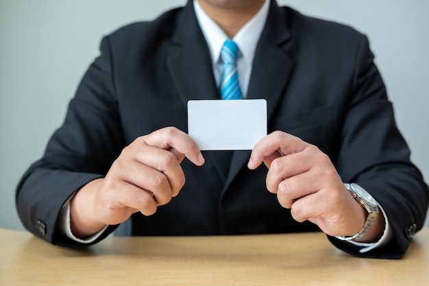 写真 ビジネスの男性は机に座って、白いカードを示すスーツを着る