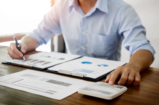 business men working on wooden desk(table) with notebook computer paper, pencil and hand in office, financial concept.