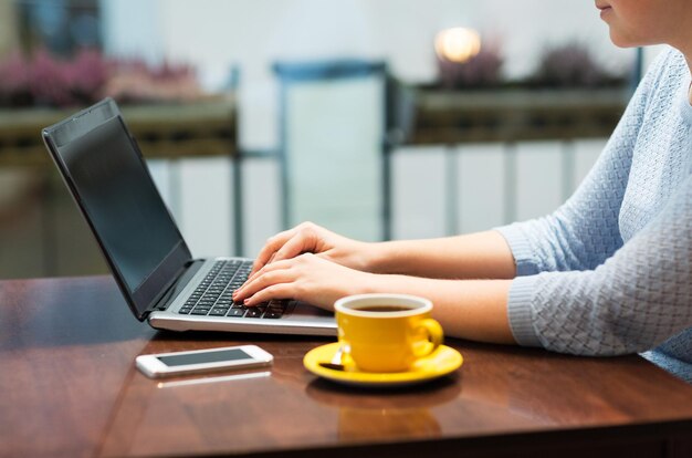 business, mensen, technologie en lifestyle concept - close-up van vrouw typen op laptop met koffie en smartphone