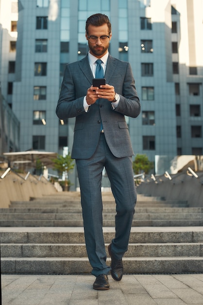 Business message full length of young and handsome businessman in formal wear using smart phone