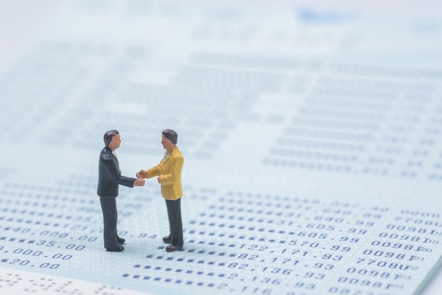 business miniature people shaking hands on book bank background