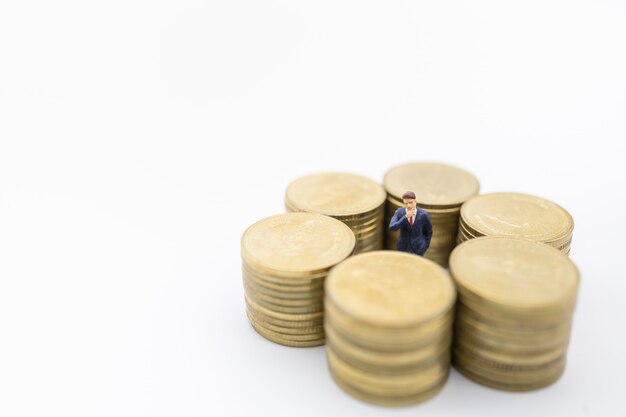 Business, money, finance and management . close up of businessman miniature figure standing center of row of stack of gold coins.