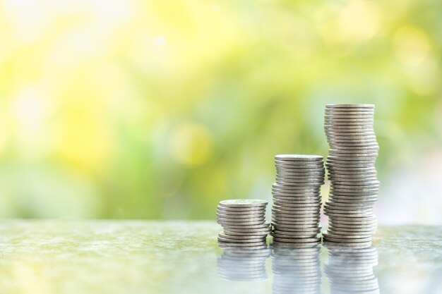 Business, Money, saving and security concept. Close up of three unstable stack of coins with bokeh of green leaf nature .