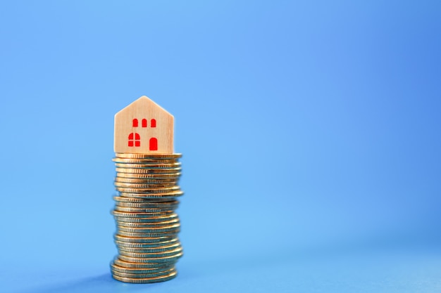 Business, Mortgage, Home Loan Concept. Closeup of wooden house block on top of stack of gold coins on blue with copy space.