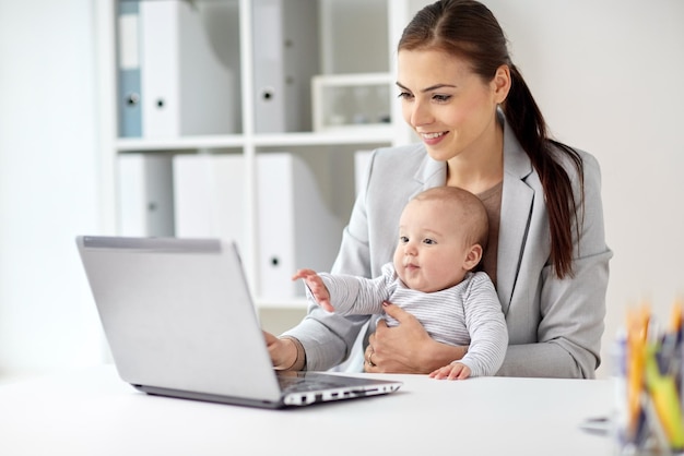 ビジネス、母性、マルチタスク、家族、人々のコンセプト – オフィスで働く赤ちゃんとラップトップコンピューターを持つ幸せな笑顔の実業家
