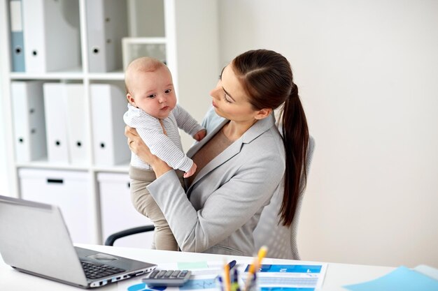 Foto affari, maternità, multitasking, famiglia e concetto di persone - felice donna d'affari sorridente con bambino e computer portatile che lavora in ufficio