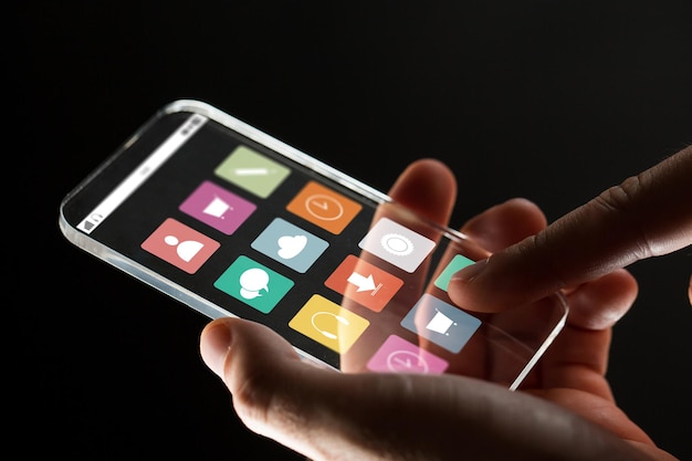 Photo business, multimedia, people and modern technology concept - close up of businessman hand with transparent smartphone with menu icons on screen over black background