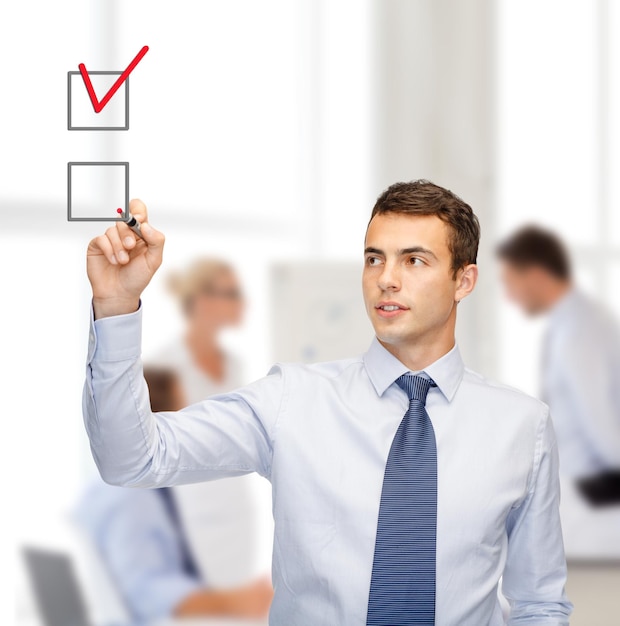 Photo business and office concept - attractive buisnessman or teacher with marker drawning red checkmark into checkbox