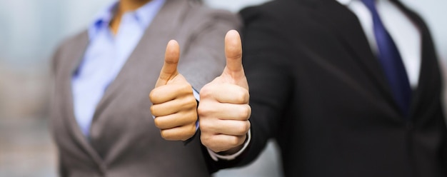 business and office concept - businessman and businesswoman showing thumbs up in office