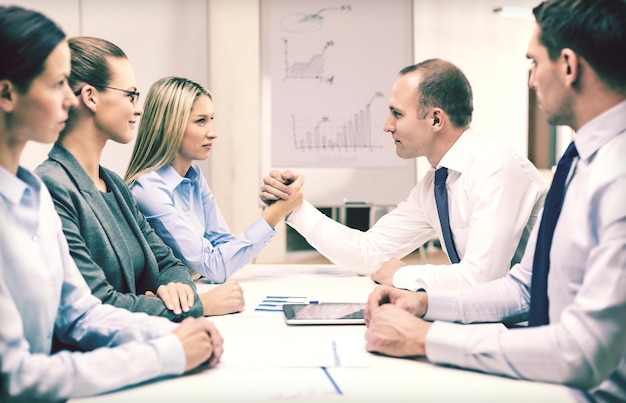 business and office concept - businesswoman and businessman arm wrestling during meeting in office