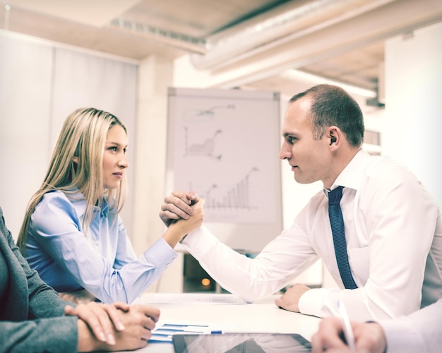 business and office concept - businesswoman and businessman arm wrestling during meeting in office