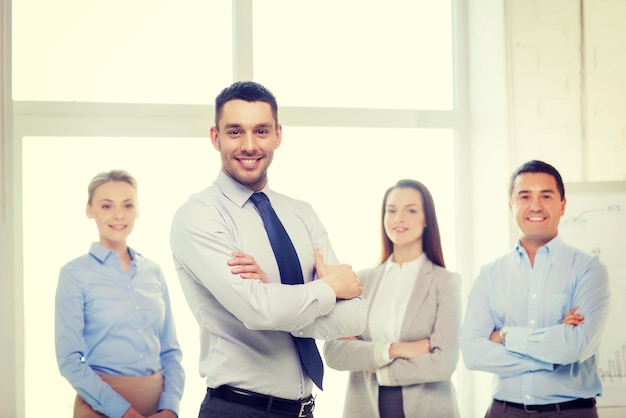 business and office concept - smiling handsome businessman with crossed hands and team in office