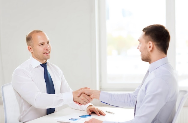 business and office concept - two smiling businessmen shaking hands in office