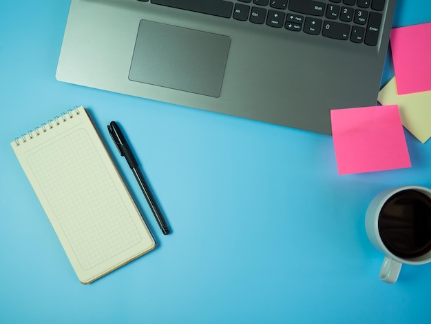 Idee di concetto di scrivania ufficio affari vista dall'alto con caffè portatile e blocco note in bianco su sfondo blu