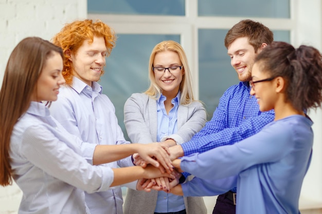 business, office, gesture and startup concept - smiling creative team with hands on top of each other sitting in office