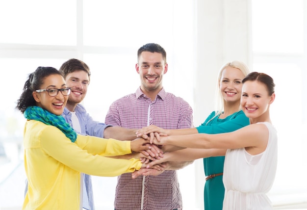 business, office, gesture and startup concept - smiling creative team with hands on top of each other sitting in office