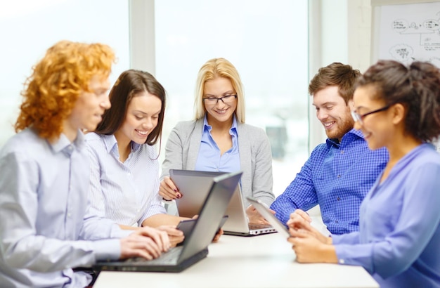 business, office and startup concept - smiling creative team with table pc and laptop computers working in office