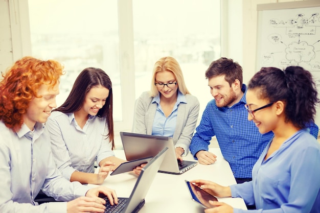 business, office and startup concept - smiling creative team with table pc and laptop computers working in office