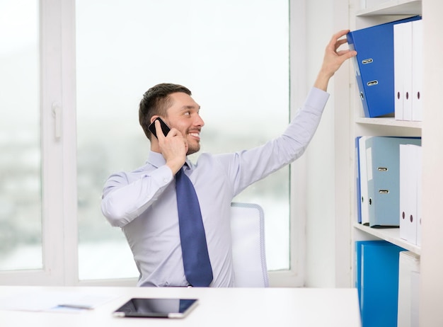 business, office and technology concept - smiling businessman with smartphone and tablet pc at office