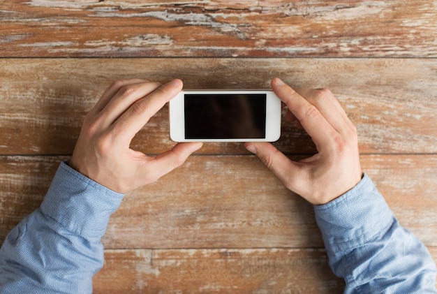 business, onderwijs, mensen en technologie concept - close-up van mannelijke handen met smartphone op tafel