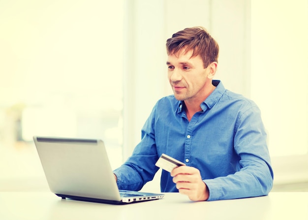 business, online banking, internet shopping concept - smiling man with laptop and credit card at home