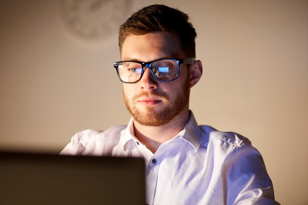 business, overwork, people, deadline and technology concept - businessman in glasses with laptop computer thinking at night office