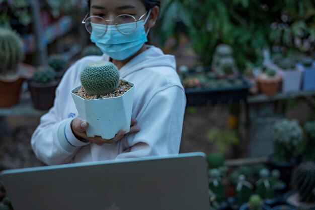 Photo business owner selling trees caring for a pretty potted cactus happy home grown  female worker working in brush planting cactus online
