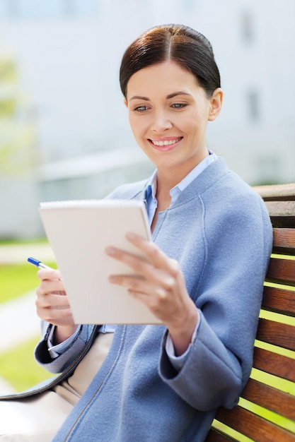 business, paperwork and people concept - young smiling businesswoman reading notes in notepad and sitting on city bench