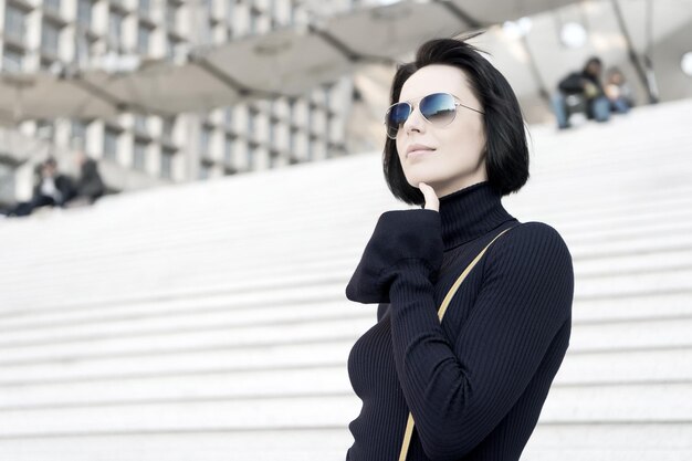 Business parisian woman with stylish short brunette hair. Girl in fashionable glasses outdoor. Beauty and urban fashion. Fashion model pose on stairs background. Look and city style, copy space