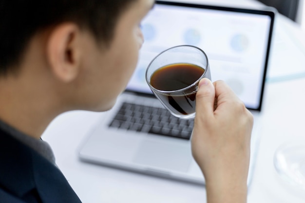 Business partners concept a young male entrepreneur holding a cup of black coffee sitting with a laptop while attending in a monthly meeting.