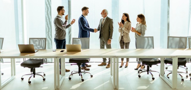 Business partners handshaking after making agreement with employees near by