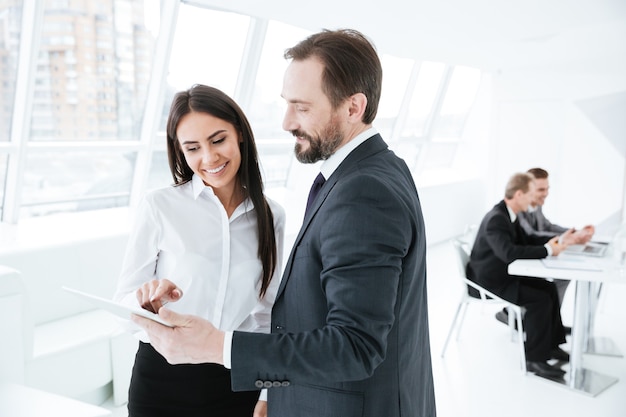 Business partners looking at tablet in office with colleagues