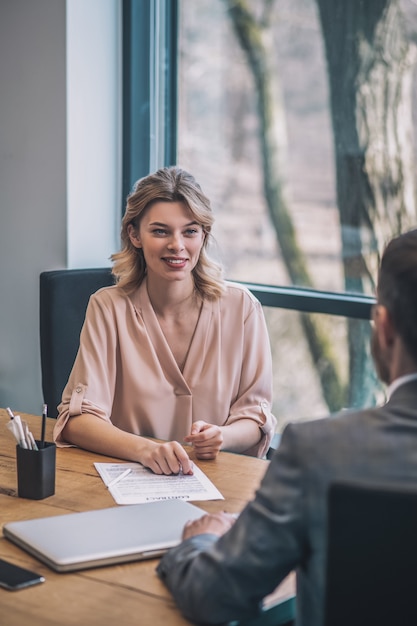 Business partners. Young joyful business woman in light blouse and man in suit with his back to camera communicating in office