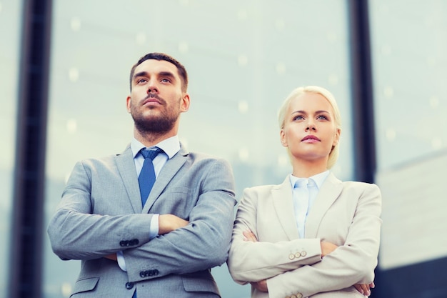 business, partnership, success and people concept - serious businessman and businesswoman standing over office building