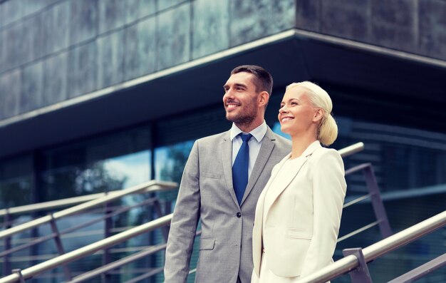 business, partnership, success and people concept - smiling businessman and businesswoman standing over office building