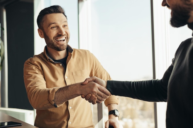 Photo business partnership two happy businessmen handshaking after successful deal at modern office