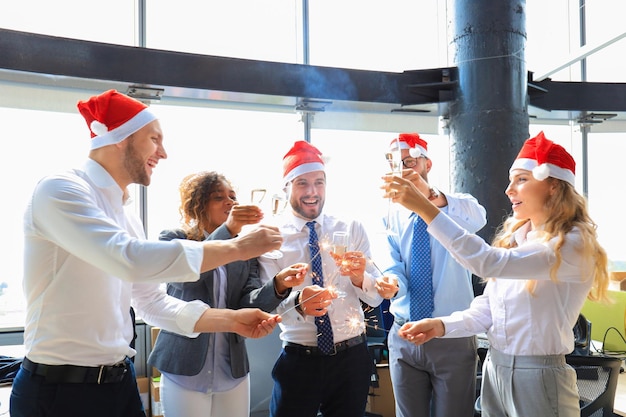 Business people are celebrating holiday in modern office drinking champagne and having fun in coworking. Merry Christmas and Happy New Year 2020.