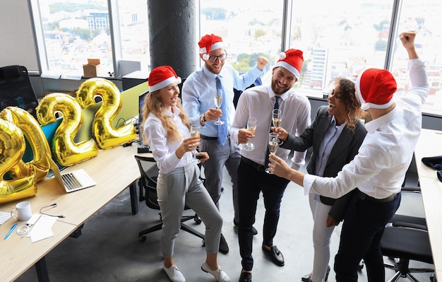 Business people are celebrating holiday in modern office drinking champagne and having fun in coworking. Merry Christmas and Happy New Year 2022.