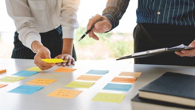 Business people arranging sticky notes commenting and brainstorming on work priorities colleague in a modern co-working space.